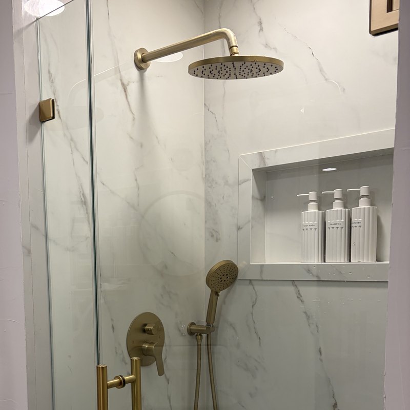 Brushed brass rain head, handheld and valve against Calacatta Oro porcelain.